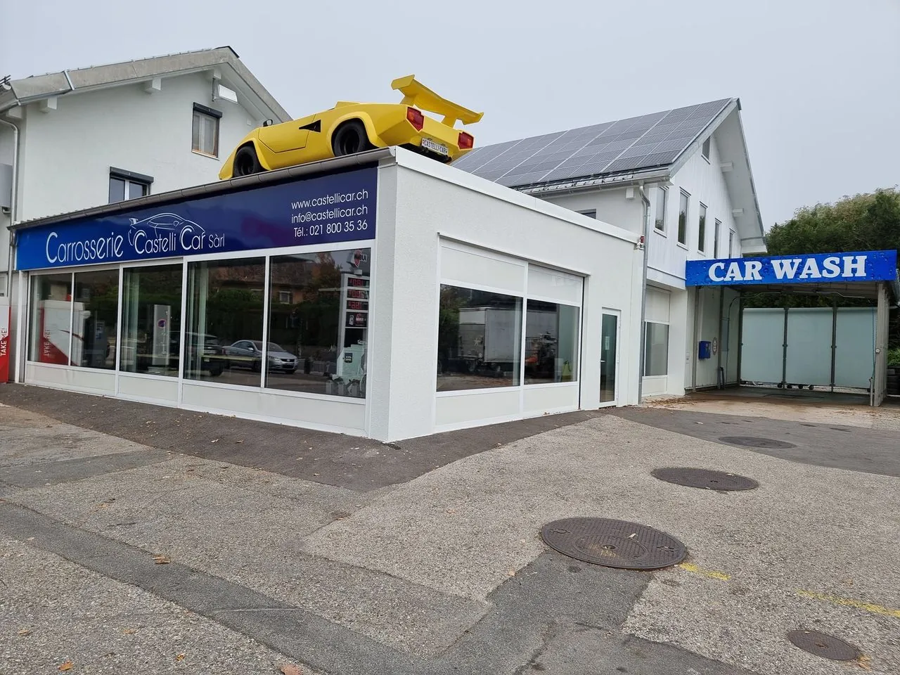 Façade de l’atelier à Cottens, voiture jaune sur le toit